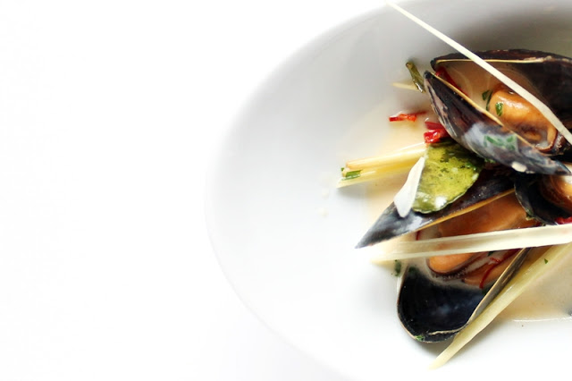 Mussels with thai flavors, from above. Part of a small bowl on white background